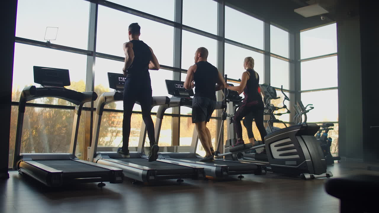 Two men running on a treadmill in the background of a large window in the fitness room. Young men running in the fitness room. Aerobic workouts in the gym.