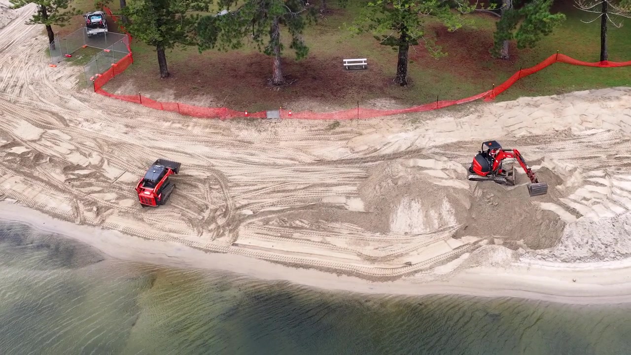 Ripresa aerea con drone di macchinari pesanti che spostano sabbia durante il ripristino di una spiaggia sul lungomare in Australia