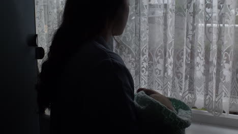 silhouette of young mother cradling her newborn baby in her arms beside windowsill and gently swaying side to side locked off