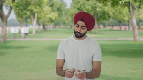 sad sikh indian man counting money in park