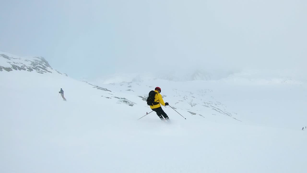 Uomo con giacca gialla scia giù per una montagna in una giornata nuvolosa a Laax, Svizzera