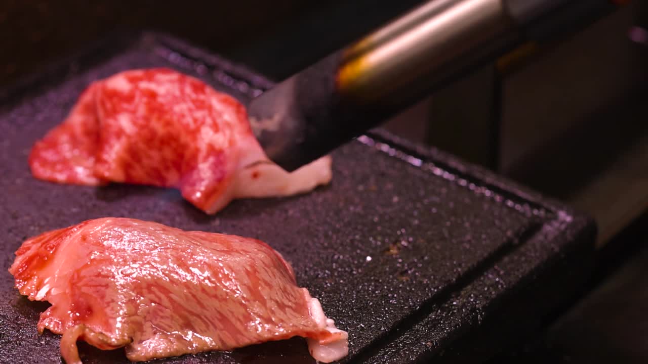 Detailed view of marbled beef slices sizzling on a hot grill with visible searing and browning.