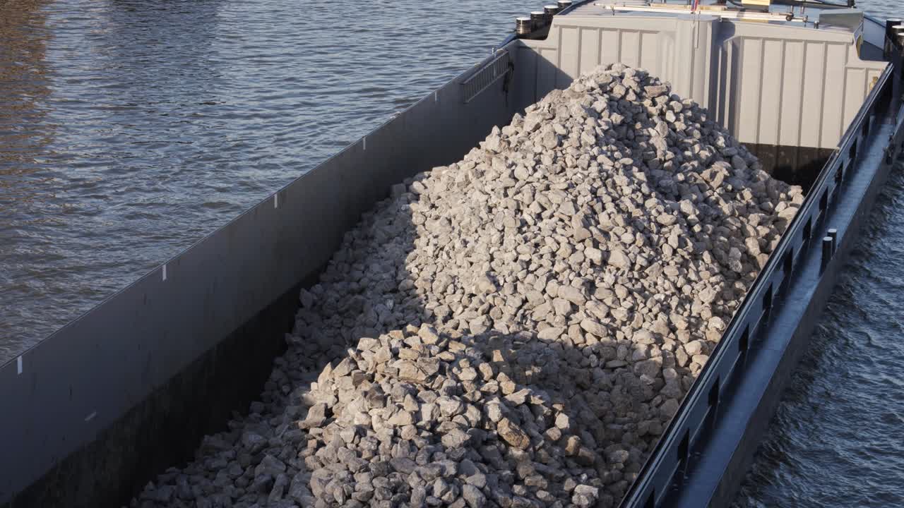 A cargo barge loaded with crushed stones sails through a canal, highlighting industrial transport, construction materials, and harbor logistics