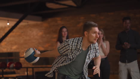 young male bowling player throws a ball with the support of friends and rejoices by knocking out a shake