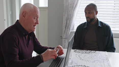 two men having a conversation at a table with a laptop