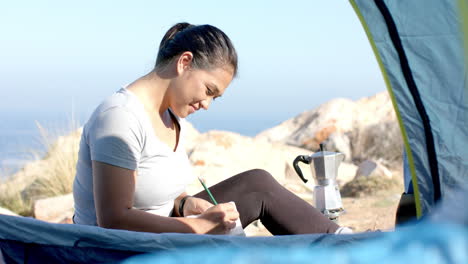 camping in mountains, woman writing in notepad outside tent, enjoying nature
