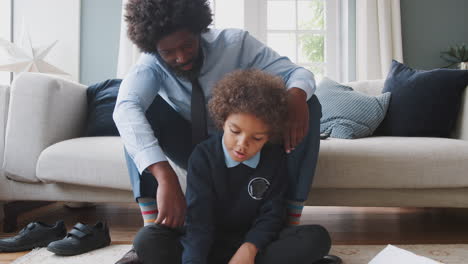 front view of pre-teen boy in school uniform sitting on the floor at home doing his homework helped by his father, sitting behind him on the sofa, zoom out shot
