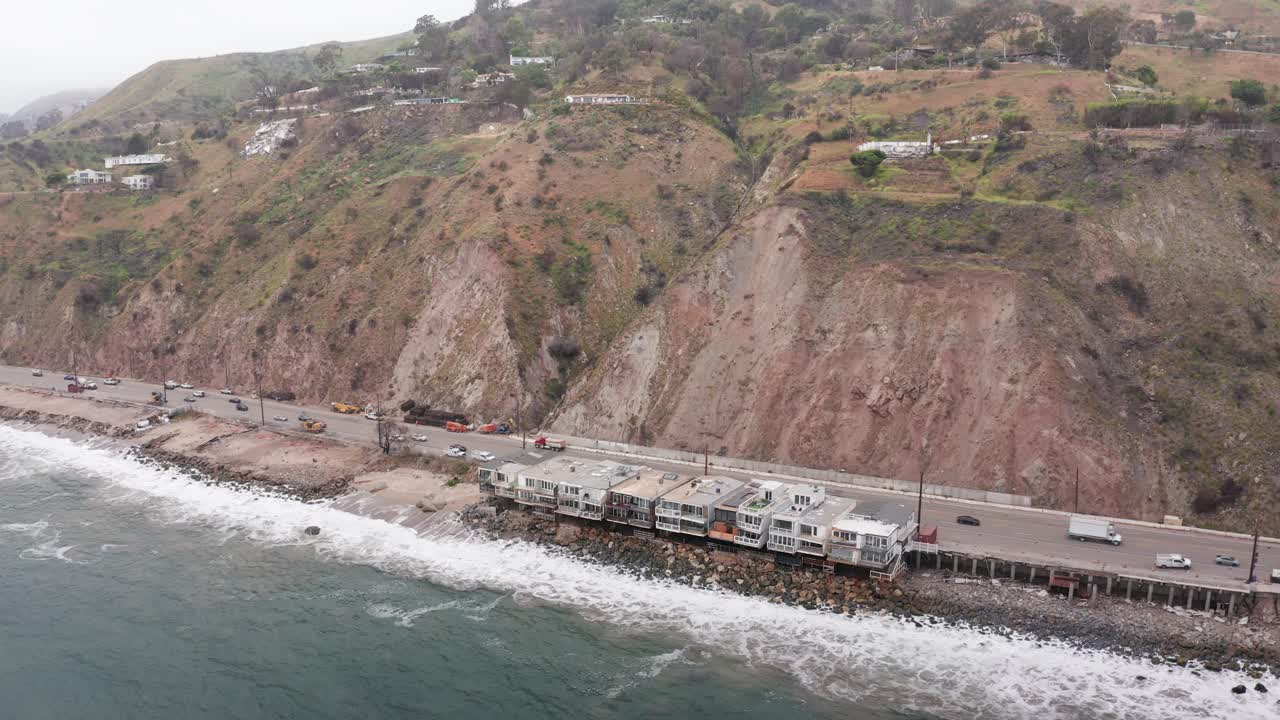 Aerial wide descending shot of surviving beachfront homes along the Pacific Coast Highway after the Palisades wildfire in Malibu, California. 4K