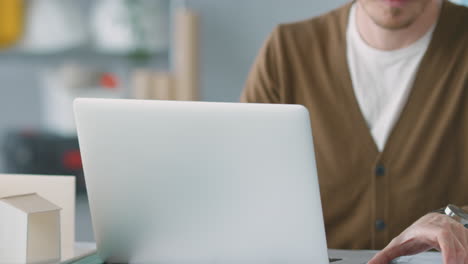 arquitecto masculino en la oficina trabajando en un escritorio en una computadora portátil tomando una llamada de altavoz en un teléfono móvil