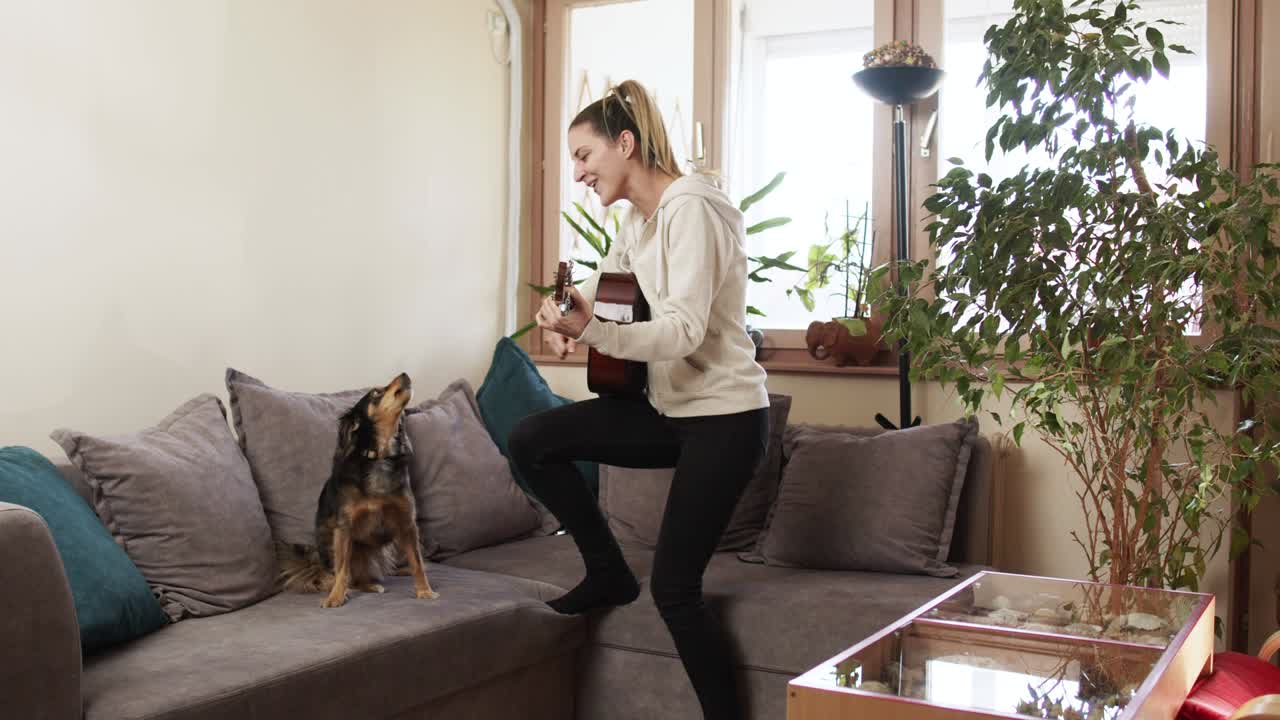 молодая женщина играет на гитаре, в то время как ее собака поет.