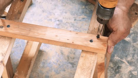 traditional carpenter drilling a crew into a piece of wood to build the legs of a chair for selling as forniture