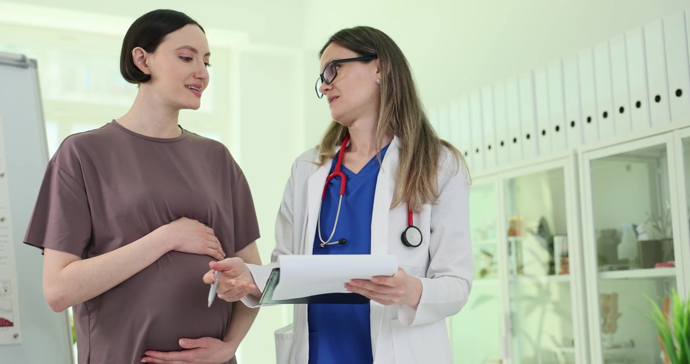 Doctor shows record on clipboard to pregnant woman in clinic
