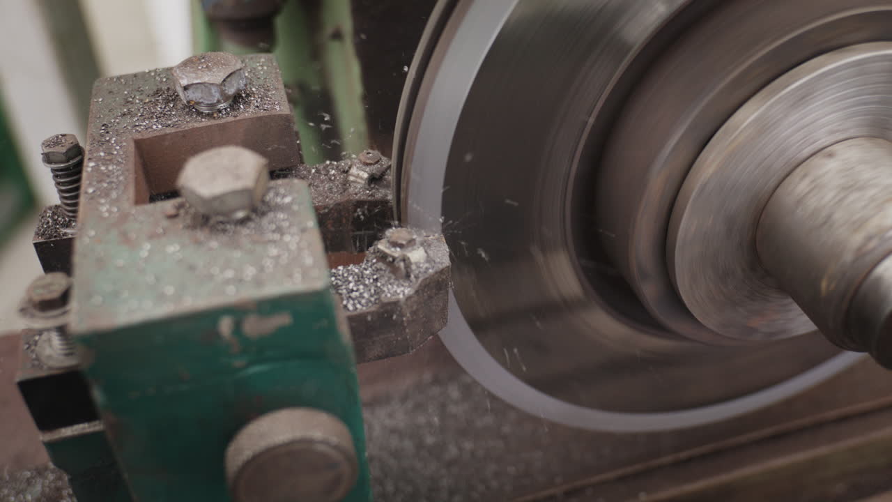 Närbild av en grön metallhyvel som bearbetar ett stålblock, vilket skapar rök och metallspån i en verkstad
