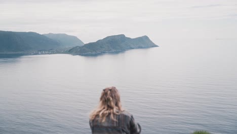 curly blonde woman sitting on island cliff side and overlooking ocean water