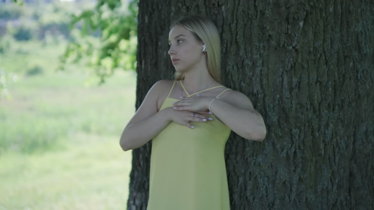 mujer con vestido amarillo bailando junto al árbol en el parque de verano