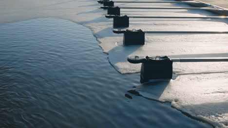 Slomo-of-water-and-snowy-ice-by-jetty-without-boats-in-sunlight