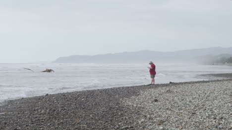 chico turista de pie en la orilla de piedras finas con olas rompiendo durante la mañana brumosa en la playa de olon, ecuador