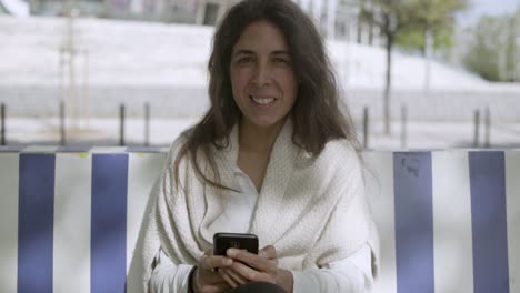 Smiling-middle-aged-brunette-holding-phone-and-looking-at-camera.