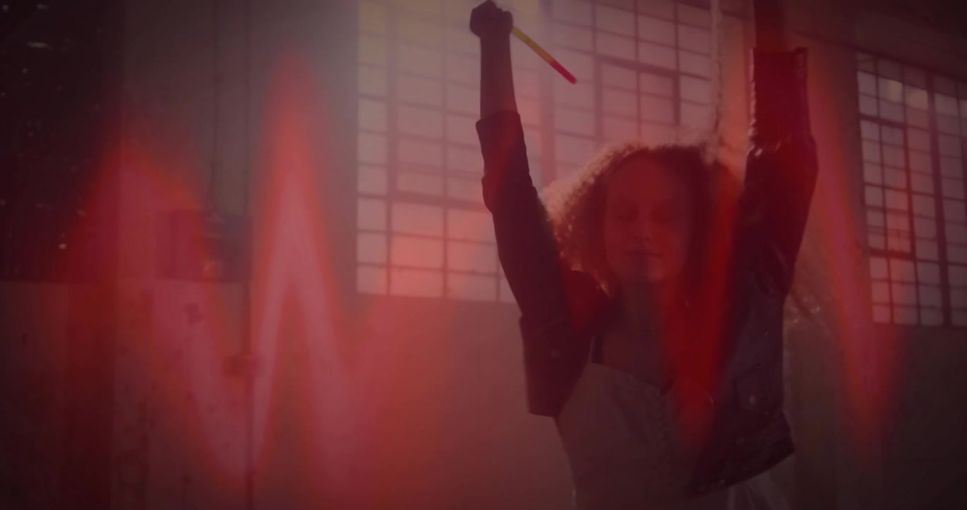 Ballerina che alza le braccia all'altezza delle spalle, attivando una forma d'onda rossa mentre fa roteare bastoni luminosi per una demo tecnologica