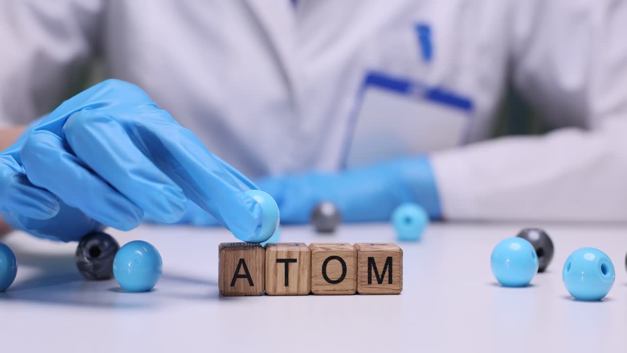 Scientist's Hand in Glove Places Atom Model on Wooden Blocks
