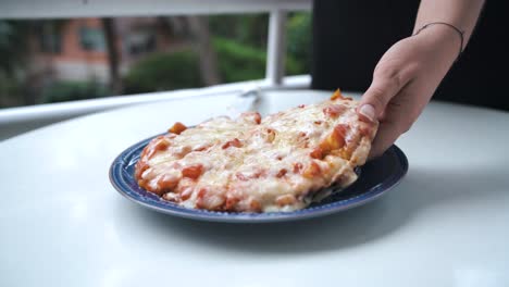 mano femenina tomando una rebanada de pizza casera con mucho queso