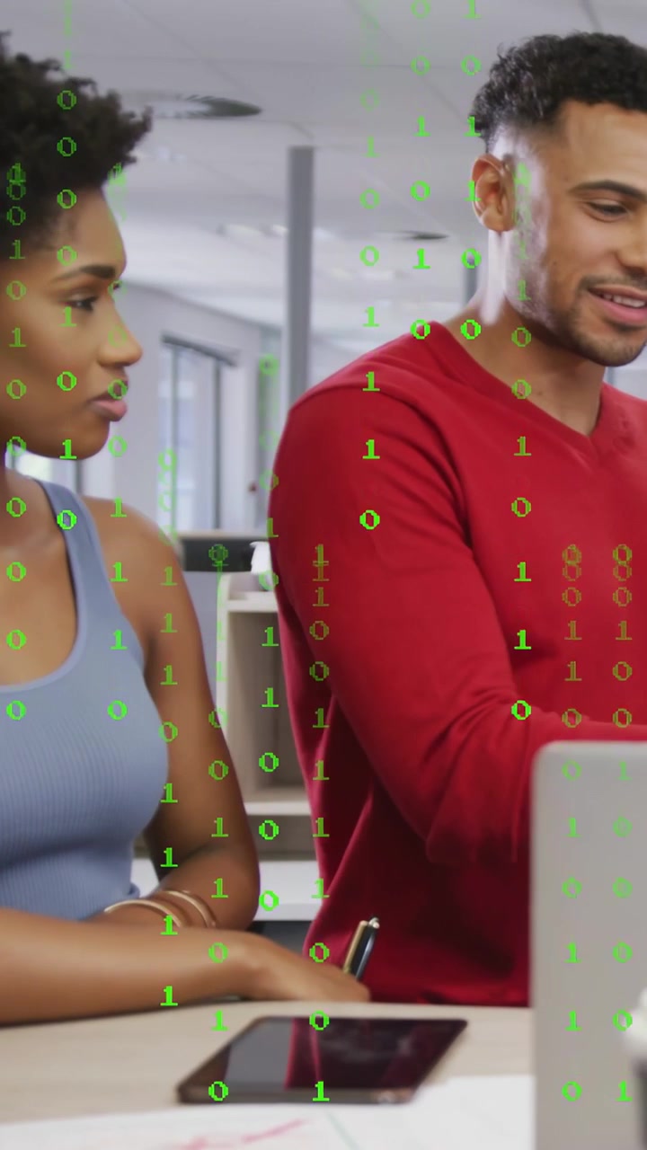 Man tapping laptop causing binary overlay over desk, woman holding pen, working on tech report