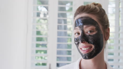 Portrait-of-happy-biracial-woman-with-beauty-face-mask-in-bathroom,-slow-motion,-copy-space