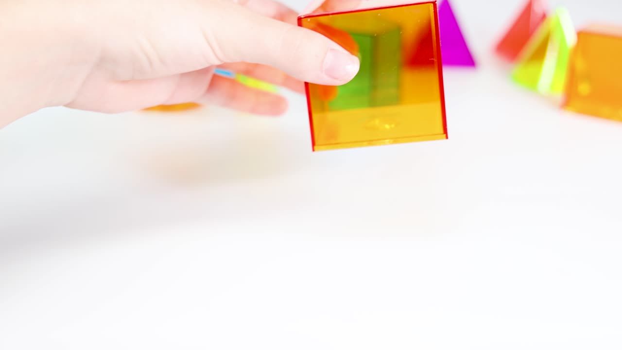 Hands manipulate colorful transparent cubes on a white surface, illustrating geometric concepts with vibrant lighting and clear focus
