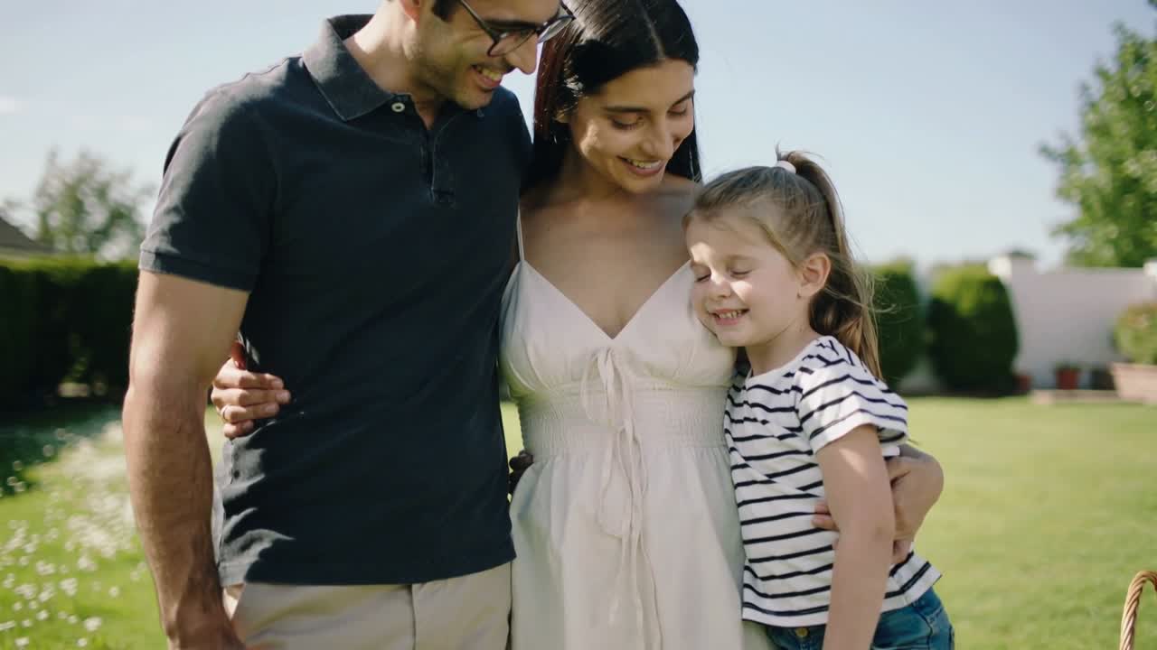 Video verticale: Luce solare che illumina la famiglia che si abbraccia sul prato, mamma in vestito chiaro, papà con occhiali, cesto.