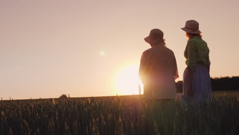 two women - mother and daughter look at the beautiful sunset over the wheat field