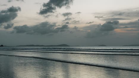 timelapse of waves swashing on long beach at dusk creating reflections of sky in sand