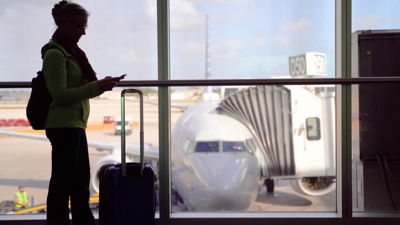 silueta de mujer sonriendo con equipaje y teléfono inteligente con avión borroso a través de la ventana exterior