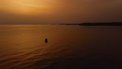 Flying-a-circle-around-a-vacation-yacht-ship-fishing-boat-by-beautiful-orange-sunset-seaside-bay-in-the-idyllic-Adriatic-mediterranean-sea-ocean-by-the-Croatian-coast