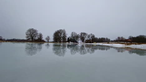 snow and ice pond on a gray day - panorama with trees reflecting off the lake's surface