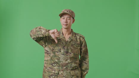 asian man soldier showing thumbs down gesture to camera while standing in the green screen background studio