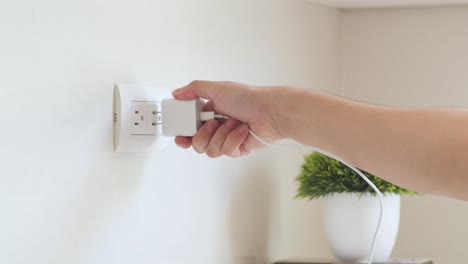 persona enchufando un cargador de teléfono en el enchufe de la pared