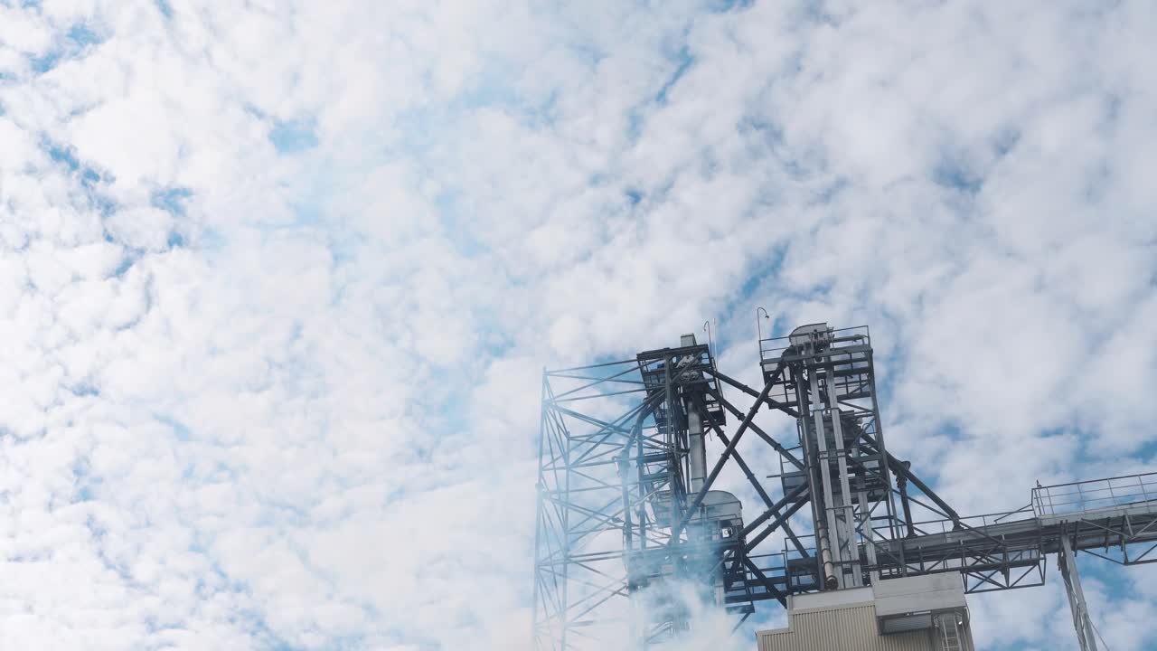 L'industria inquina l'atmosfera. Vapore bianco di un essiccatore di grano si disperde nell'aria. Alto impianto industriale su sfondo cielo.