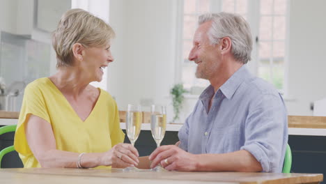 kissing retired couple celebrating with glass of champagne at home on date night together