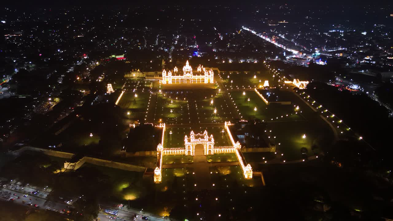Aerial view of Mysuru Palace illuminated at night, surrounded by sparkling city lights. Highlights the grandeur and cultural richness of Karnataka's iconic royal landmark. India.