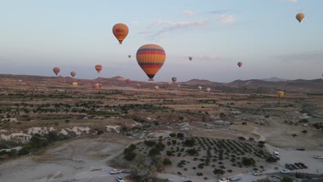 Drone-view-of-touristic-balloons-flying-in-the-valley,-Nevsehir-hot-air-balloon-tours-in-skyscape