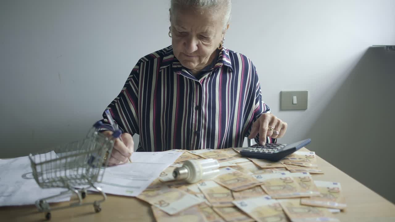 Ældre kvinde tjekker regninger, betaler forbrugsregninger med euro og pære, beregner pengebesparelser på skrivebordet derhjemme