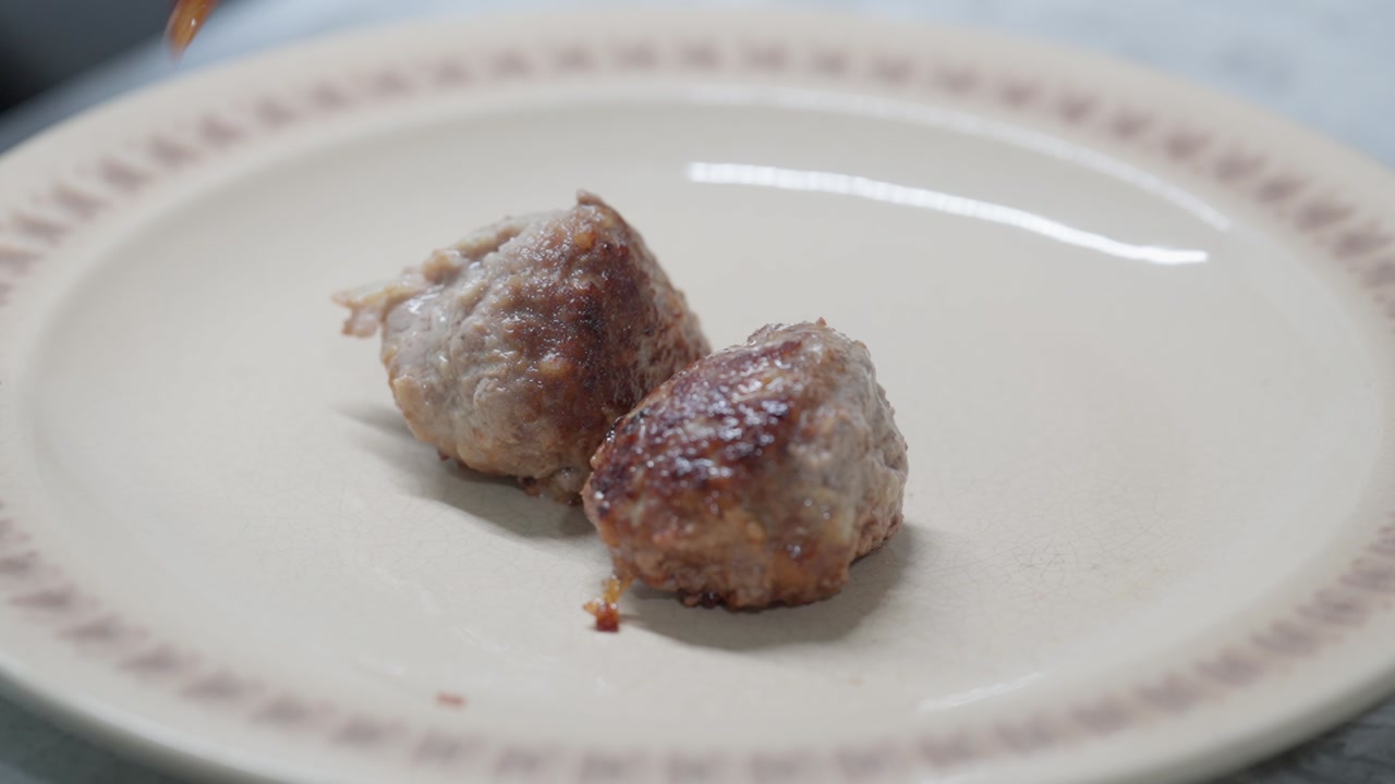 Close-up of cooked meatballs being placed onto a clean plate for serving.