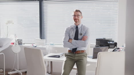 Portrait-Of-Smiling-Mature-Male-Doctor-Sitting-On-Desk-In-Office