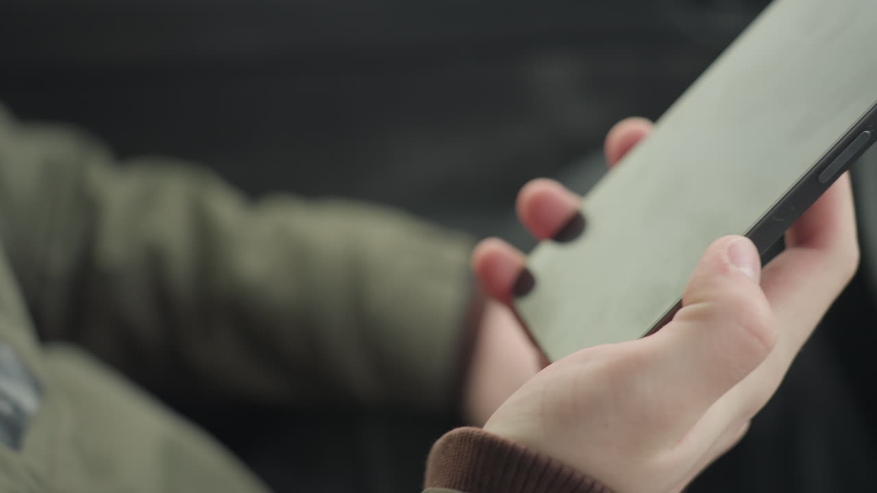 close up of young boy in winter jacket holding smartphone with both hands while making phone call inside parked car, blurred cold weather background