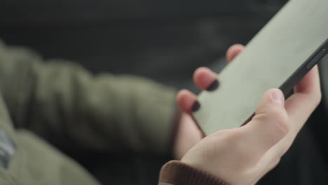 close up of young boy in winter jacket holding smartphone with both hands while making phone call inside parked car, blurred cold weather background
