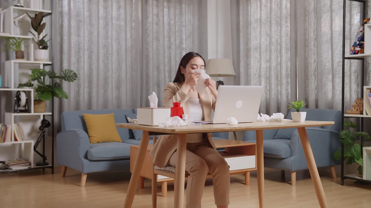 아픈 아시아 사업가 여성이 집에서 거실에서 노트북으로 일하면서 아픈 소녀는 재채기를 고 을 조직으로 습니다.