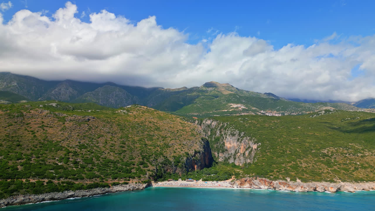 알바니아의 gjipe 해변과 캐니언 위에서 뒤로 움직이는 항공 드론은  ⁇ 은 날 배경에서 지나가는  ⁇  구름과 함께  ⁇ 습니다.