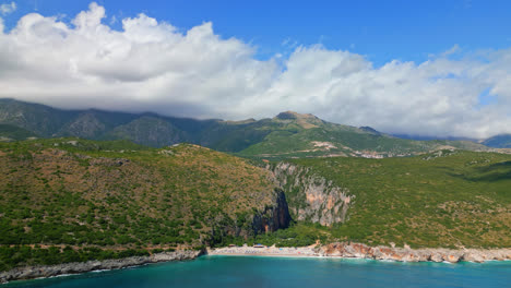 drone aéreo moviéndose hacia atrás disparado sobre la playa y el cañón de gjipe en albania con nubes blancas pasando en el fondo en un día soleado