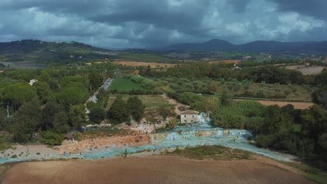 Luftaufnahmen-Der-Ikonischen-Thermalquellen-Von-Saturnia-Cascate-Del-Mulino-Mit-Ihrem-Blauen,-Warmen-Wasser-In-Der-Idyllischen-Und-Romantischen-Landschaft-Der-Toskana,-Italien,-Mit-Feldern-Und-Olivenbäumen