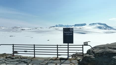 Cartel-En-La-Cima-Del-Paso-De-Montaña-De-Sognefjellet-Informando-Sobre-La-Altitud-De-1428-Metros-Sobre-El-Nivel-Del-Mar---Fondo-Nevado-Durante-El-Verano